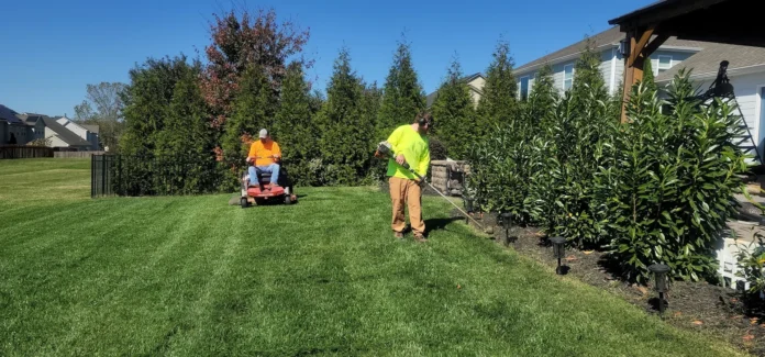 Professional lawn care workers maintaining a lush green residential yard with a mower and trimmer