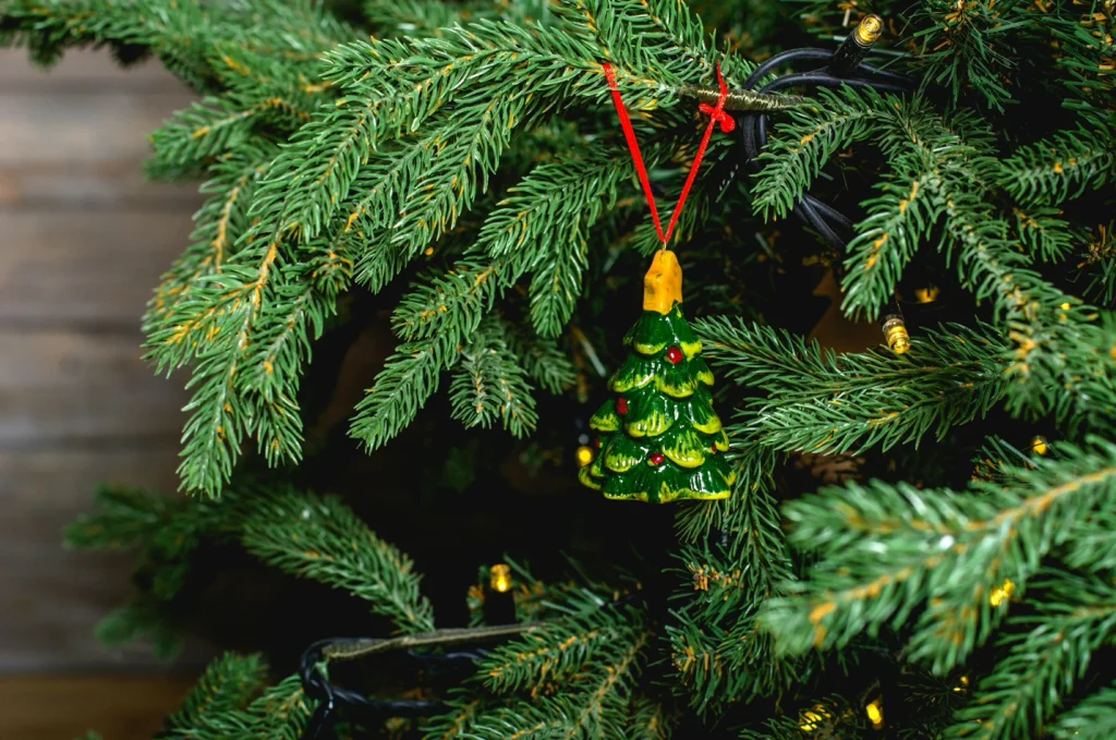 Close-up of a handmade ornament hanging on pine branches with lights, showcasing creative Christmas Tree Decor Ideas.