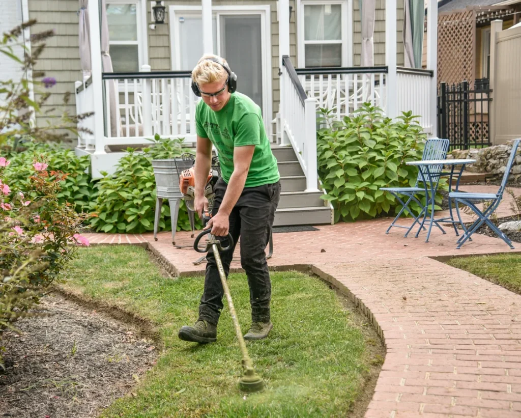 Professional lawn care worker using a string trimmer to edge a residential lawn