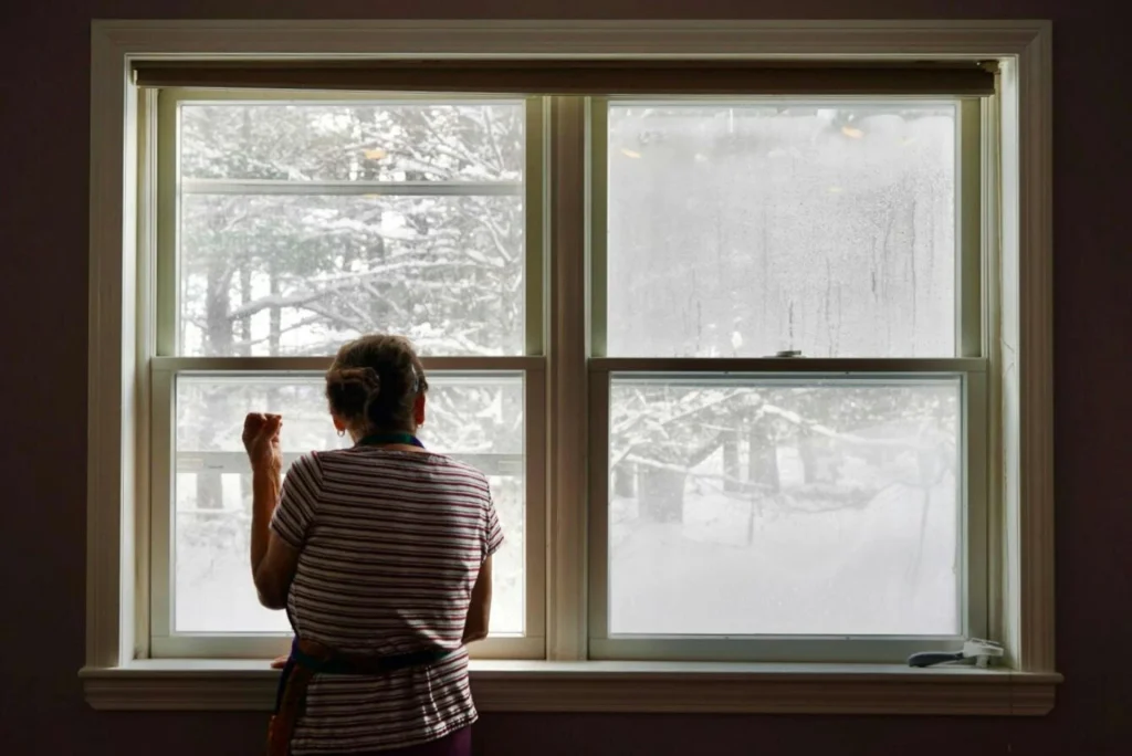Person looking out a cold, frosty window in winter to show how to keep your home warm and seal drafts.