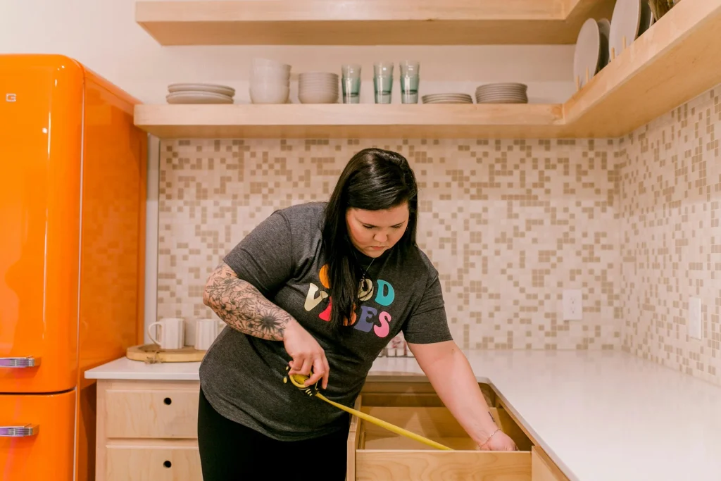 A person using a tape measure to check cabinet dimensions as part of planning how to choose furniture for your home.