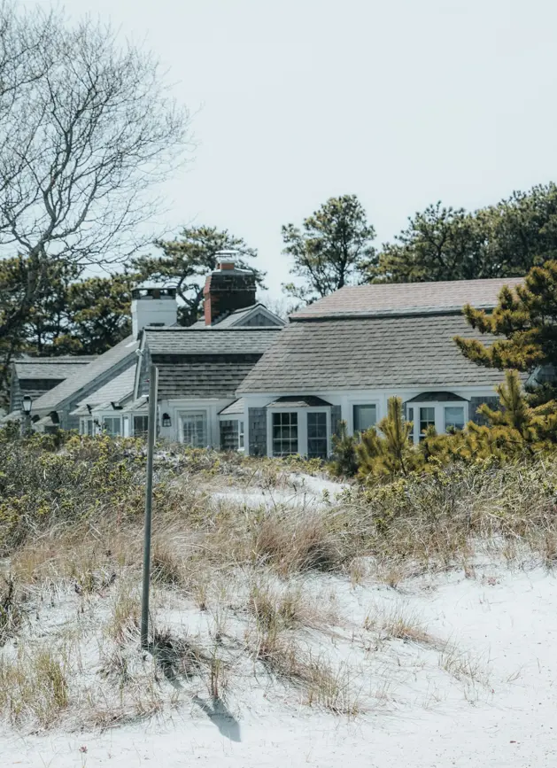 Coastal properties with shingle siding and cottage-style architecture nestled behind sandy dunes